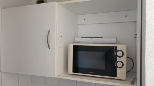 A microwave oven placed inside a white cabinet with a handle. - The Cozy Apartment in Avignon (Avignon)