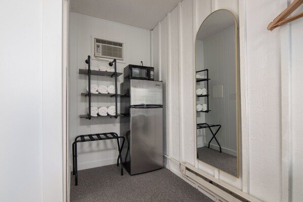 A compact kitchenette with a stainless steel refrigerator, a microwave, and a small shelf unit with towels.