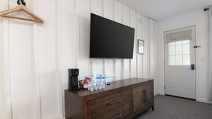 Een kamer met een wandgemonteerde flatscreen televisie, een houten kast met lades, een deur met een raam en een kapstok aan de muur.