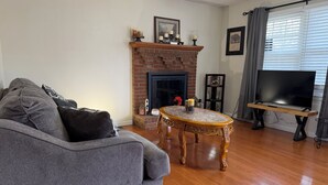 Ein Wohnzimmer mit grauem Sofa, einem Holztisch, einem Kamin aus Ziegelsteinen und einem Flachbildfernseher.