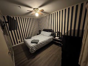 A bedroom with a bed, a ceiling fan, a nightstand, and a striped wall. - Modern 1BR Snowcrest Condo: 5-Min Walk to Soaring Eagle Lift (Snowshoe)
