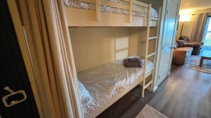 Een stapelbed met een ladder, een klein tafeltje en een bank in een kamer met een houten vloer.