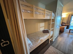 A bunk bed with a ladder, a small table, and a sofa in a room with a wooden floor. - Modern 1BR Snowcrest Condo: 5-Min Walk to Soaring Eagle Lift (Snowshoe)