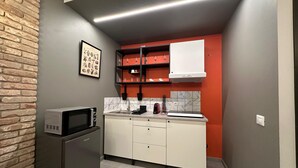 A compact kitchen with a microwave, a sink, and a stove. There is a brick wall on one side and a red accent wall above the cabinets. - Silent Airport Room 5 minutes from BGY airport and Bergamo city center (Azzano San Paolo)