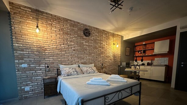 A bedroom with a brick wall, a bed with white linens, a nightstand, and a small table with a lamp. - Silent Airport Room 5 minutes from BGY airport and Bergamo city center (Azzano San Paolo)