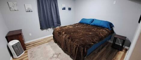 A bedroom with a bed, a heater, a rug, and a window with curtains.