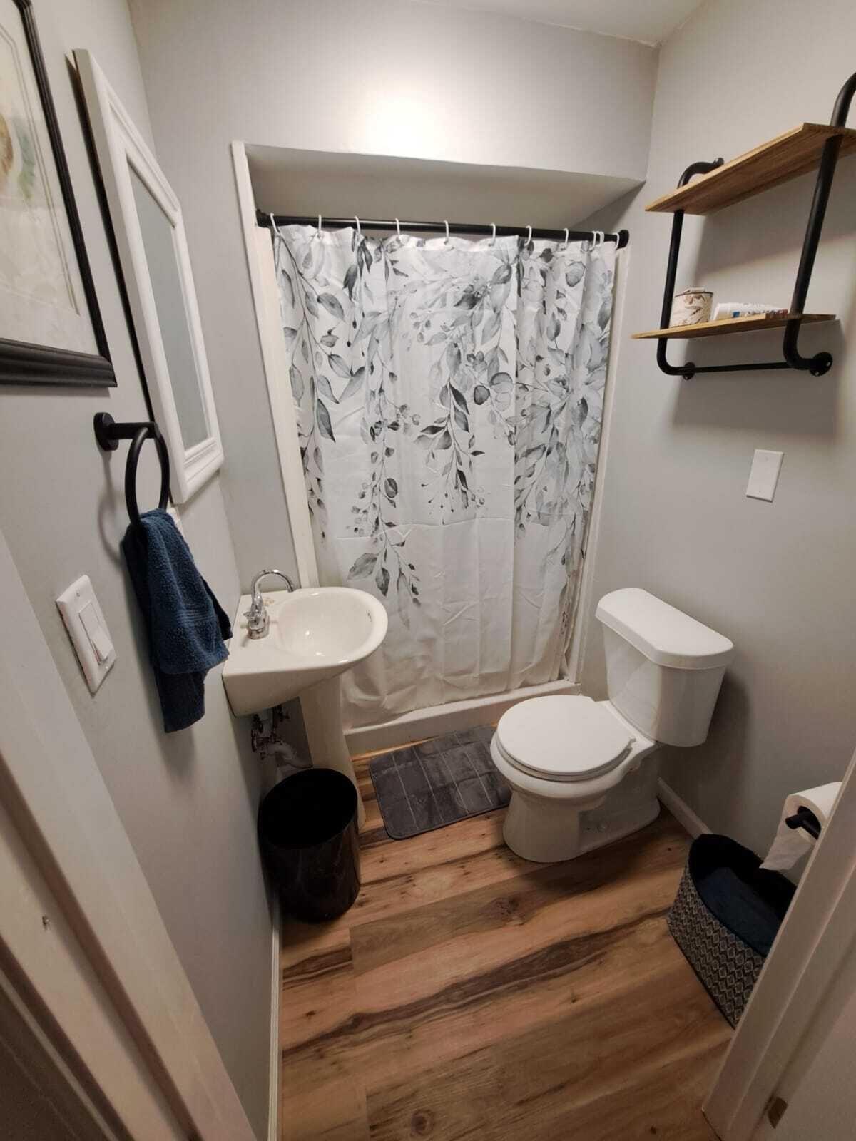 Une petite salle de bain avec un rideau de douche, des toilettes, un lavabo et un plancher en bois.