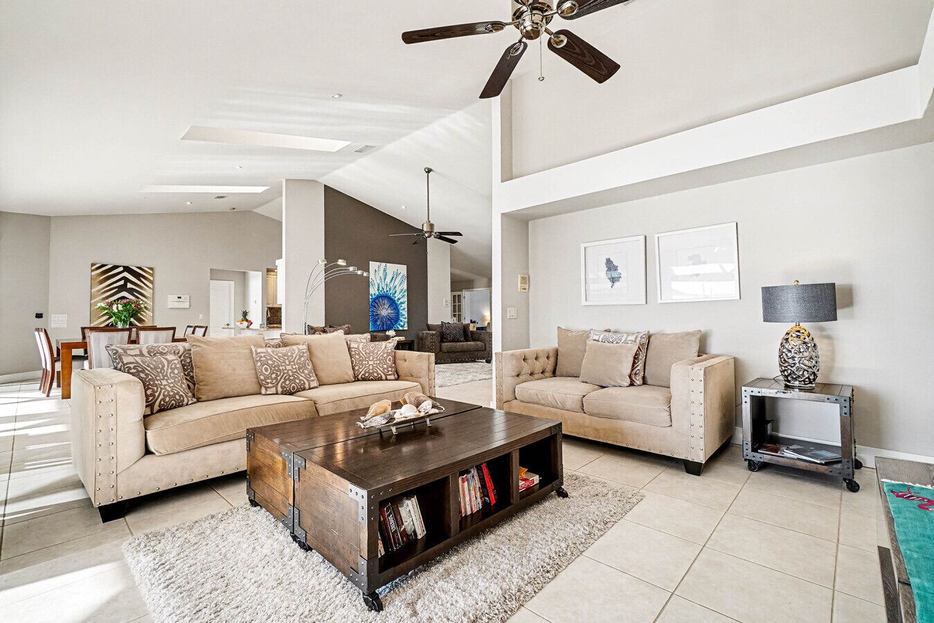 A spacious living room with a high ceiling, a ceiling fan, and a dining area in the background.