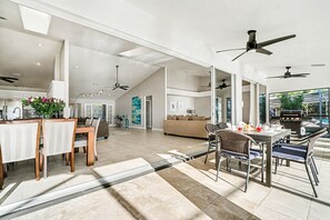 A spacious open-plan living area with a dining table, chairs, a sofa, and a kitchen area with a grill. - Villa Riverside – Luxury Riverfront Home w/ Dock, 2 Boat Lifts, Heated Pool & Whirlpool (Cape Coral)