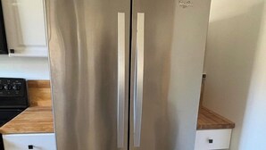 A stainless steel Whirlpool refrigerator in a kitchen with white cabinetry and a wooden countertop. - River Valley House Paradise (pigeon forge)