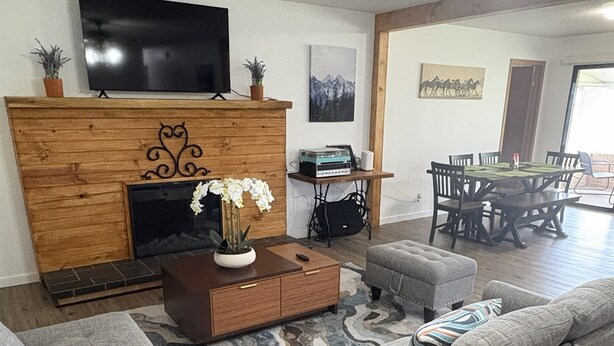 A living room with a sectional sofa, a wooden entertainment unit with a flat-screen TV, a fireplace, and a dining area with a table and chairs. - River Valley House Paradise (pigeon forge)