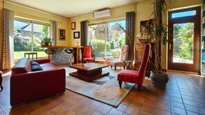 A spacious living room with a red sofa, a coffee table, and a large window offering a view of the garden. - Charming country home (Aigurande)