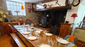 A dining area with a long wooden table set for a meal, surrounded by colorful chairs, a stone wall, and a fireplace. - Charming country home (Aigurande)