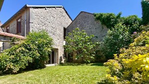 A stone building with a sloped roof, a small entrance, and a well-maintained lawn with various shrubs and a yellow flowering plant. - Charming country home (Aigurande)