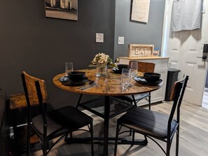 Uma mesa de jantar redonda com cadeiras pretas, um vaso com flores e uma placa na parede com a palavra 'EAT'.