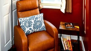 A corner room with a brown leather armchair, a window with beige curtains, a white door, and a small table with books. - Modern Designed DTWN Condo with a 99% Walk Score (Atlanta)