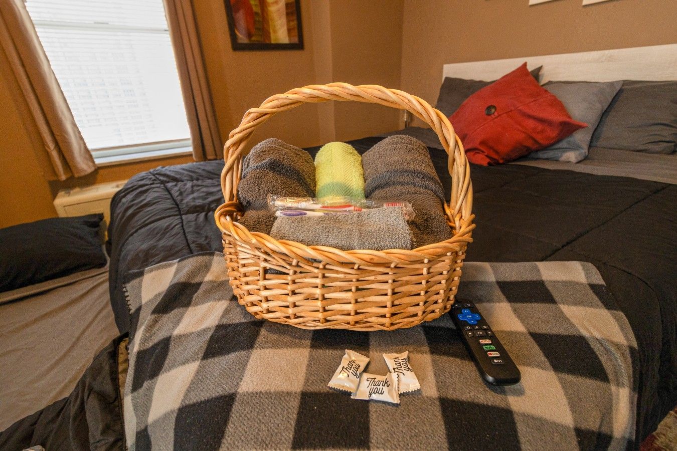A room with a bed, a basket on the bed, and a remote control.