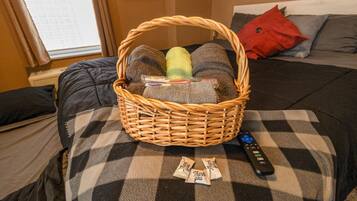 A room with a bed, a basket on the bed, and a remote control.
