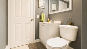 A bathroom with a white toilet, a sink, a mirror, and a door. - Modern Designed DTWN Condo with a 99% Walk Score (Atlanta)