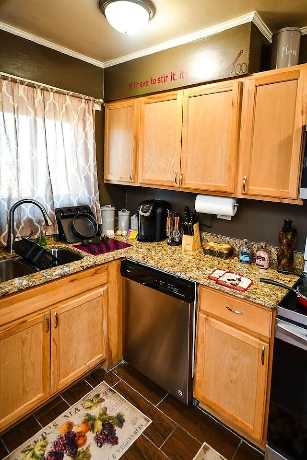 A compact kitchen with wooden cabinets, a stainless steel dishwasher, and a granite countertop.