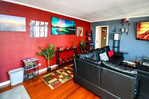 A living room with a black leather sofa, a red wall, and a blue wall with artwork. - Modern Designed DTWN Condo with a 99% Walk Score (Atlanta)