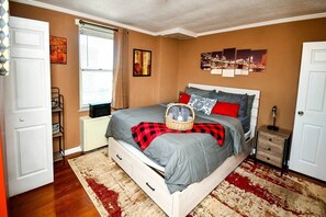 A bedroom with a bed, a bedside table, a lamp, a window, and artwork on the wall. - Modern Designed DTWN Condo with a 99% Walk Score (Atlanta)