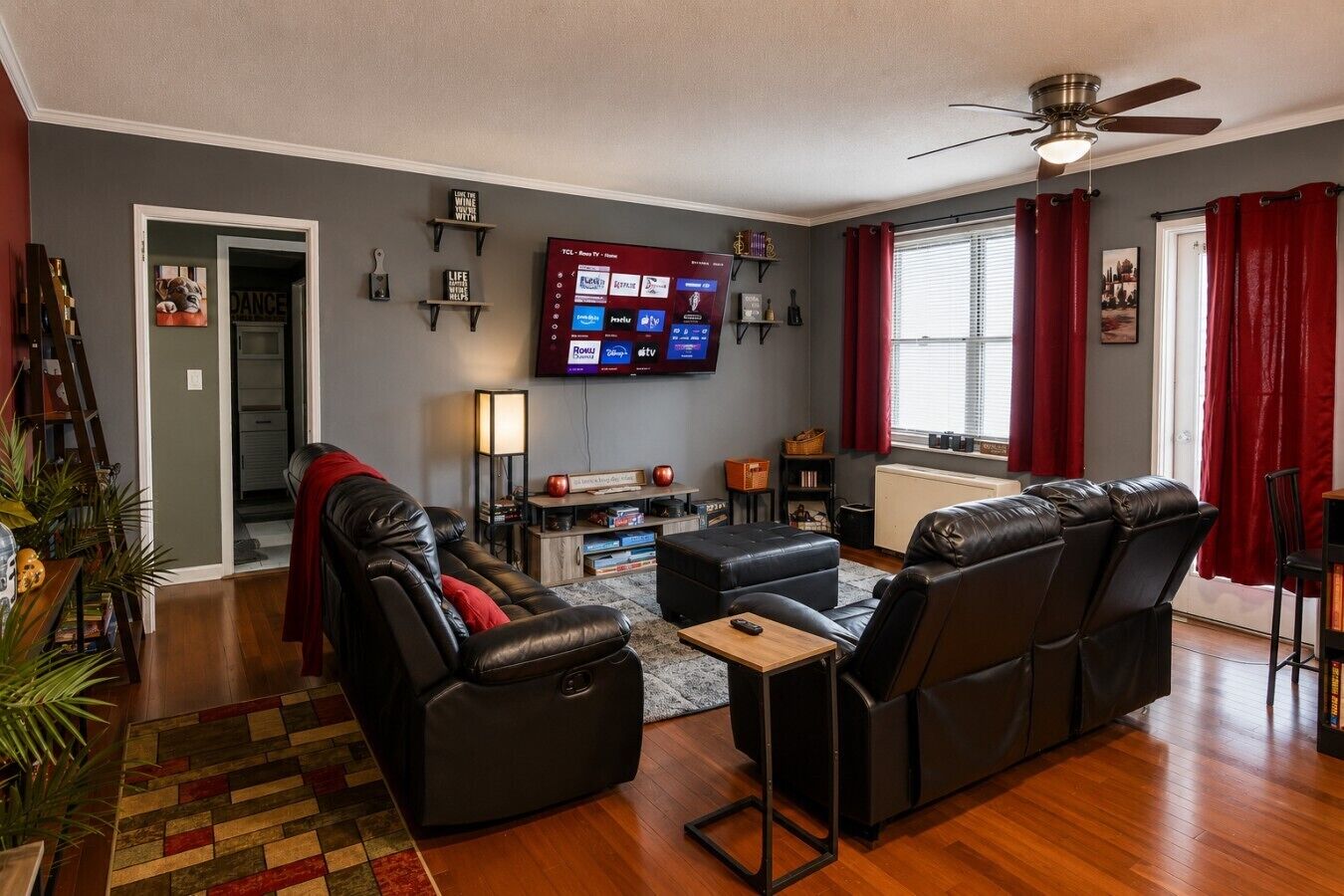 A living room with a flat-screen TV, leather sofas, a coffee table, and a red rug.