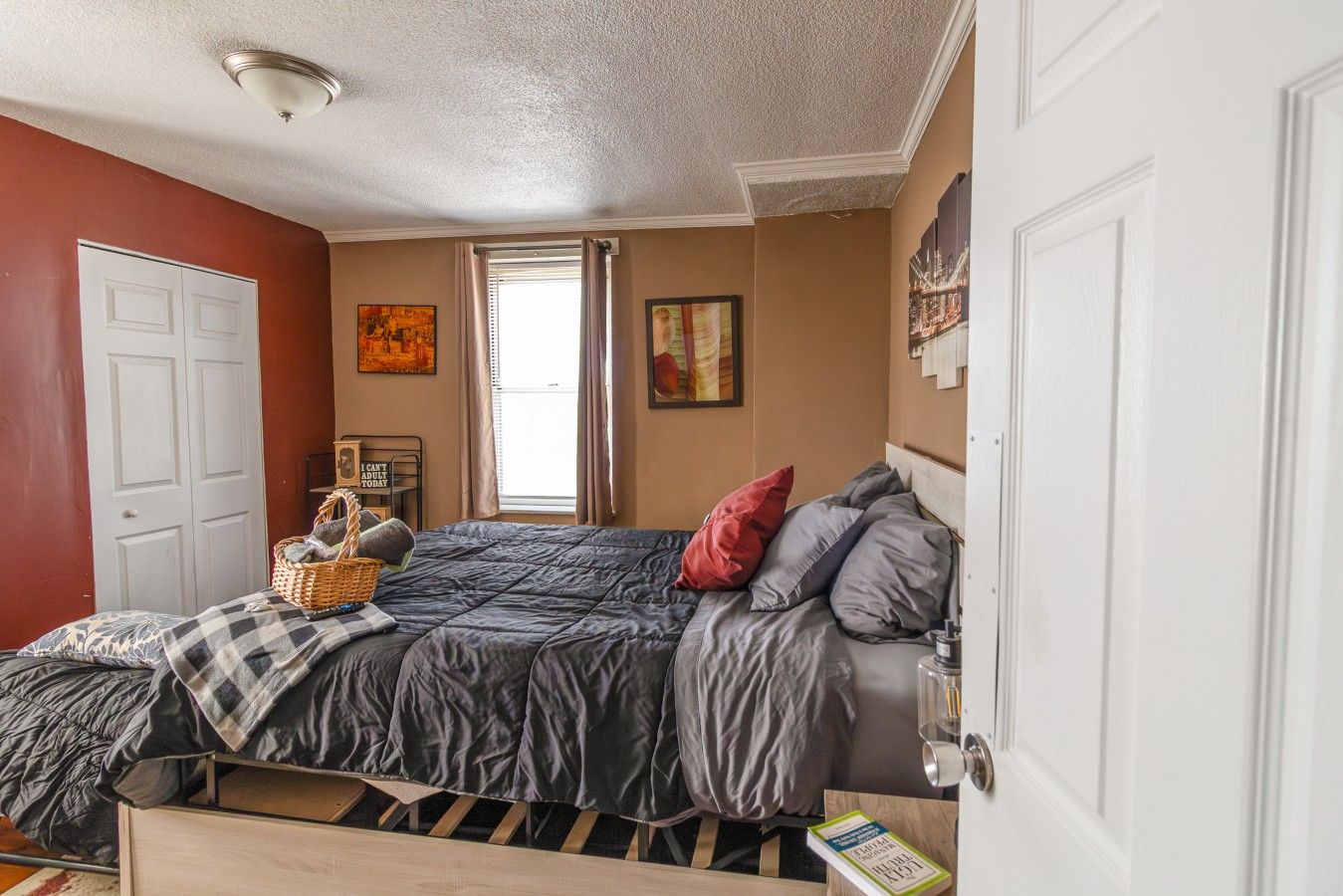 A bedroom with a bed, a window, a door, and a wall with artwork.