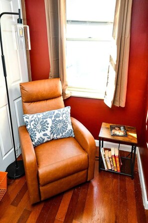 A corner room with a brown leather armchair, a small wooden side table with books, a window with curtains, and a radiator. - Modern Designed DTWN Condo with a 99% Walk Score (Atlanta)