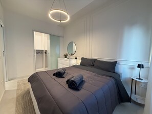 A modern bedroom with a large bed, a bedside table, a mirror, and a wardrobe.