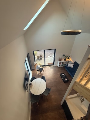 A modern living room with a dining area, a staircase, and a large window.