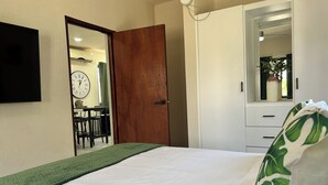 Un dormitorio con cama, puerta de madera, armario blanco, espejo y un reloj en la pared.