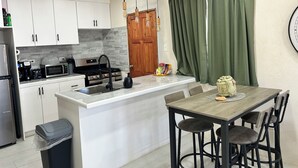 Una cocina moderna con armarios blancos, una isla central y un comedor con mesa de madera y taburetes de bar.