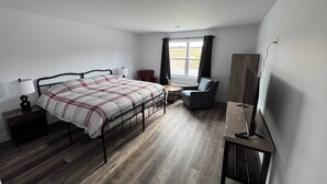 A bedroom with a bed, bedside table, lamp, chair, and a desk with a chair.