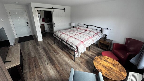 A bedroom with a bed, a desk, a chair, a small table, and a wardrobe.