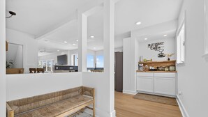 A modern interior with a wooden bench, a kitchen with white cabinets, and a wall sign that reads "BUT FIRST Coffee". - Family Waterfront Vacation Estate in New London, CT. (New London)