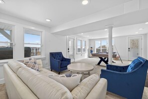 A spacious living room with a beige sofa, blue armchairs, and a pool table.