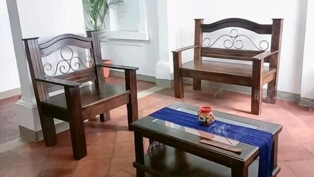 A room with two wooden chairs and a small table, a potted plant, and a white wall with an arched window. - Hotel Posada Casa Santorini (Antigua Guatemala)