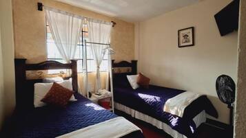 A room with two beds, a window with curtains, a bedside table, and a wall-mounted fan.