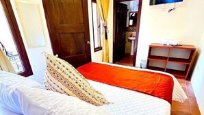A hotel room with a bed, a small table, a TV, and a bathroom visible through an open door. - Hotel Posada Casa Santorini (Antigua Guatemala)