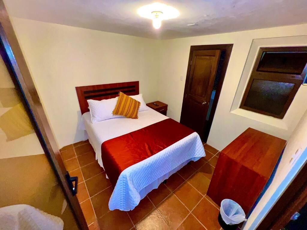 A bedroom with a bed, a wooden headboard, a nightstand, a door, and a window.