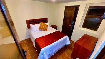 A bedroom with a bed, a wooden headboard, a nightstand, a door, and a window.