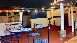 An outdoor patio area with a round table and blue chairs, surrounded by potted plants and string lights. - Hotel Posada Casa Santorini (Antigua Guatemala)