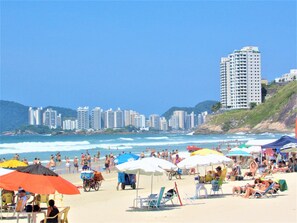 A beach with multiple umbrellas, beach chairs, and people. - Apartamento Inteiro 1 Dormitório Com Garagem Guarujá Enseada (Guarujá)