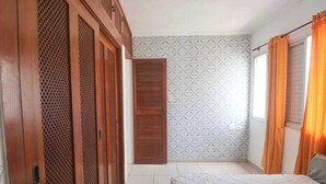 Ein Schlafzimmer mit Bett, Kleiderschrank, Tür und einem fensterbehangenen Fenster.