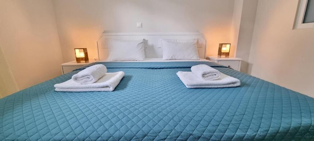 A hotel room with a blue quilted bedspread, two neatly folded white towels, and bedside lamps.