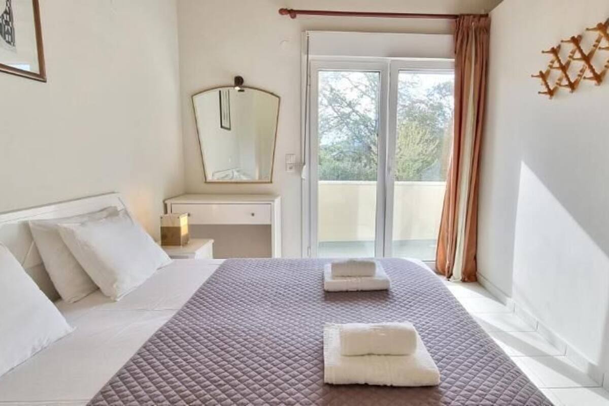 Een hotelkamer met een bed, nachtkastje, spiegel en uitzicht op het buitenleven.