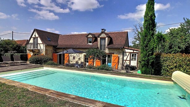 Una casa de dos pisos con piscina, balcón y un árbol alto.