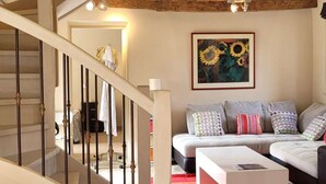 Una escalera con vigas de madera, un sofá con cojines estampados y un cuadro de girasoles.