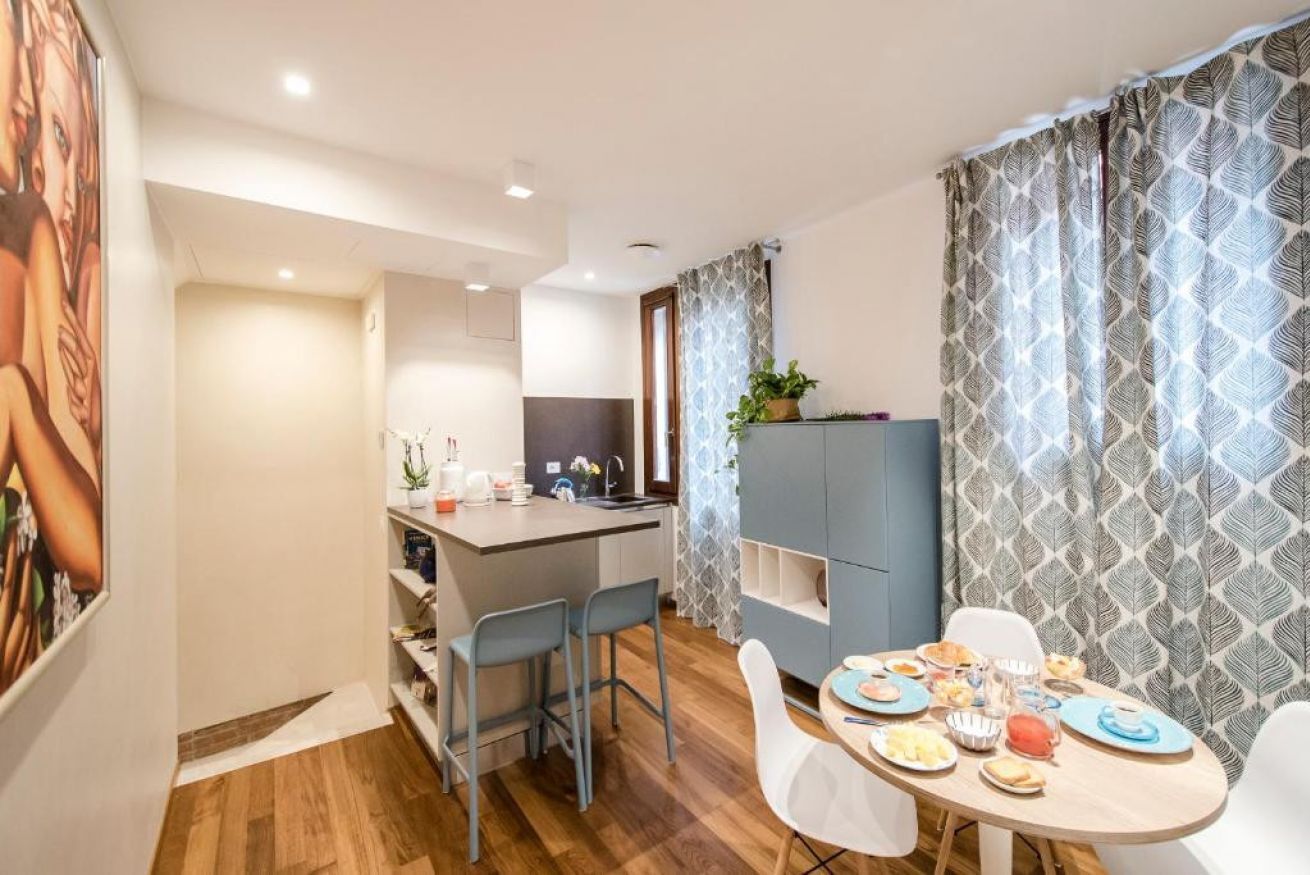 A modern kitchen with a central island, a dining area with a round table, and a living space with a sofa and a TV.